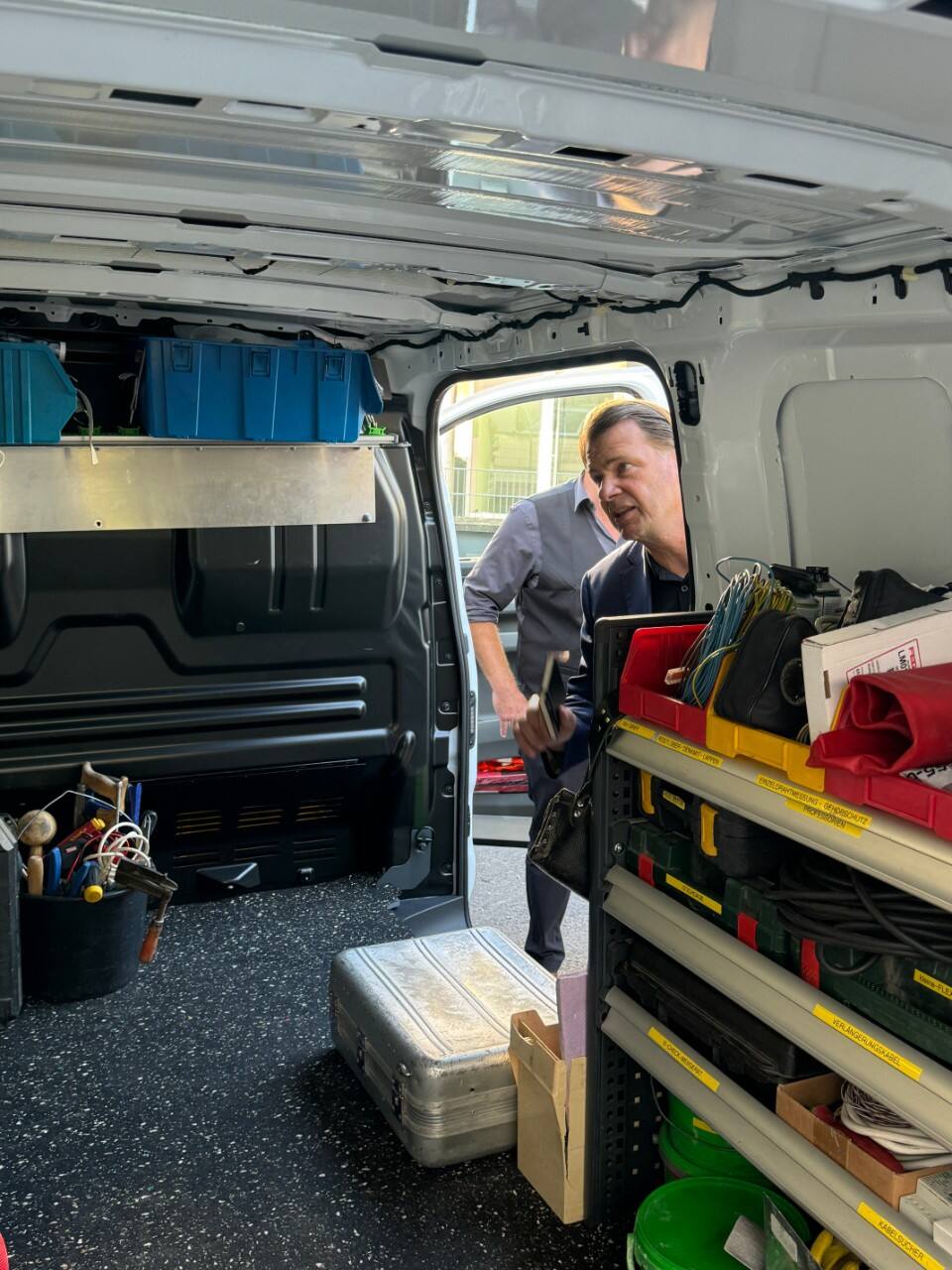 A man looks into the back cargo area of an E-Transit van. 